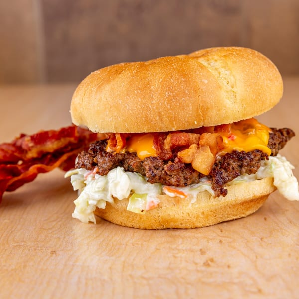 Home Run Burger's cheeseburger with bacon, coleslaw, and a side of bacon on a wooden surface.