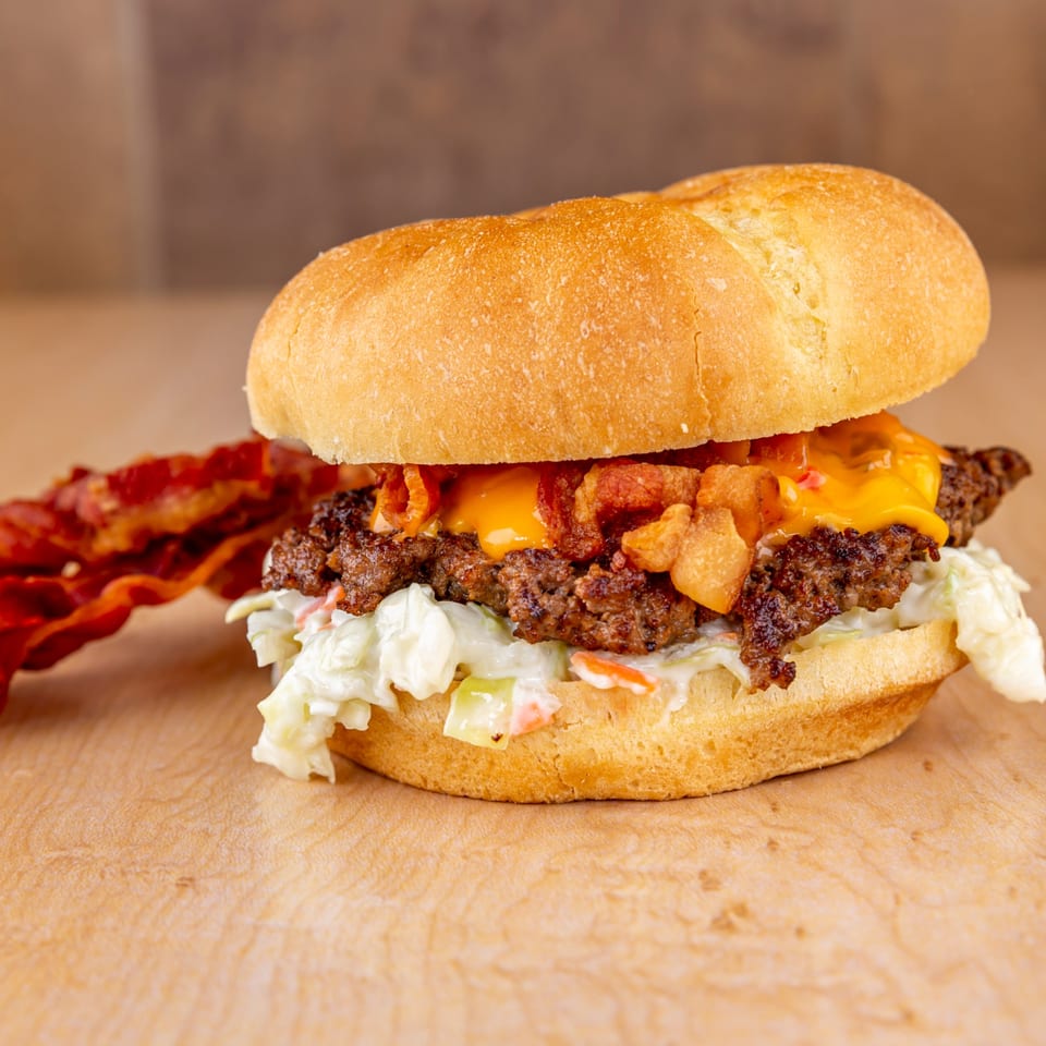 Home Run Burger's cheeseburger with bacon, coleslaw, and a side of bacon on a wooden surface.