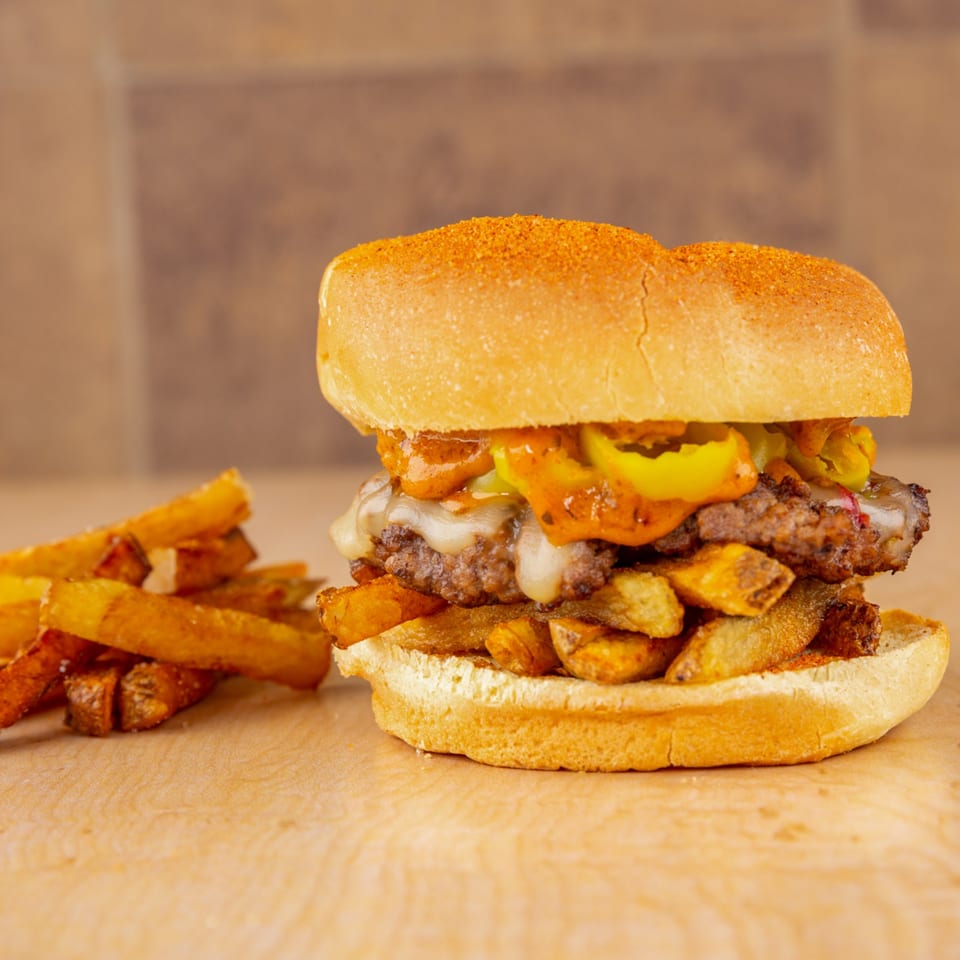 A Home Run Burger with melted cheese, peppers, and fries on a wooden surface.