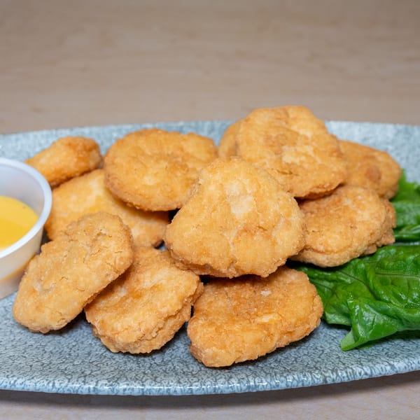 Golden-brown chicken nuggets with a side of dipping sauce and lettuce on a gray plate.