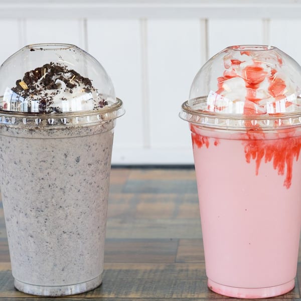 Two milkshakes, one cookies and cream, one strawberry, with whipped cream and toppings.