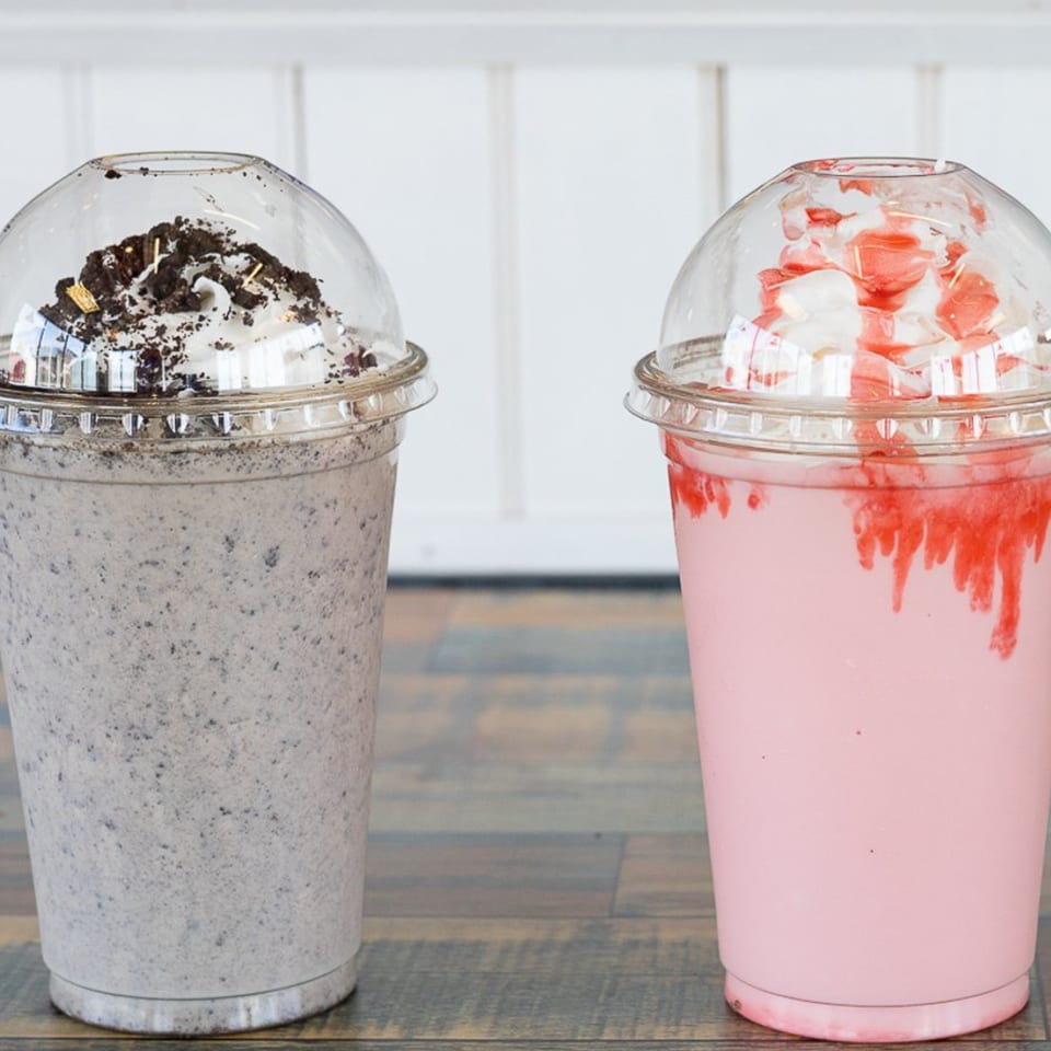 Two milkshakes, one cookies and cream, one strawberry, with whipped cream and toppings.
