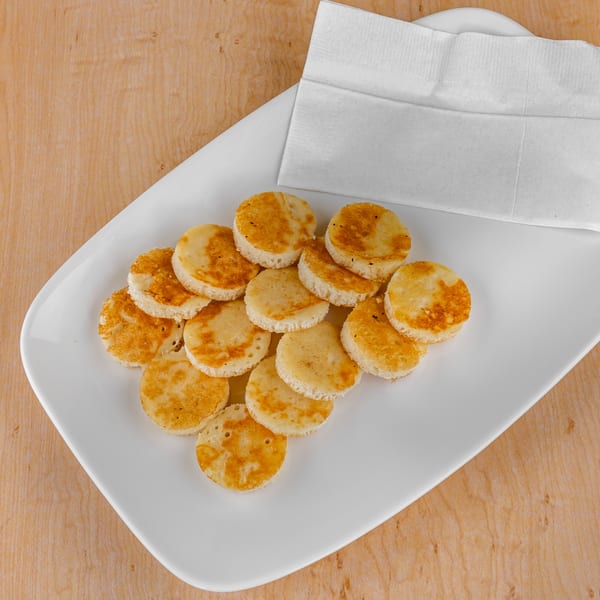 A white plate holds several small, round, golden-brown pancakes next to a folded white napkin.