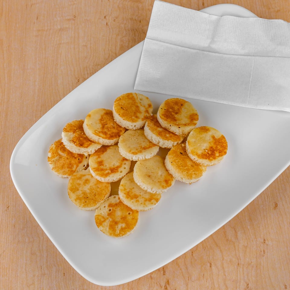 A white plate holds several small, round, golden-brown pancakes next to a folded white napkin.