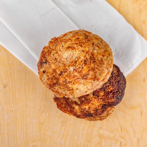Two grilled Home Run Burger patties, one slightly charred, on a white napkin and wooden surface.