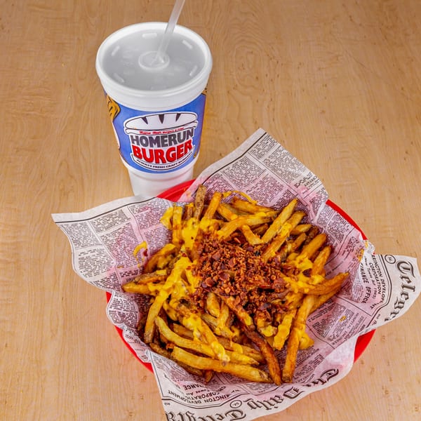 Home Run Burger's cheesy bacon fries in a red basket with a branded soda cup.