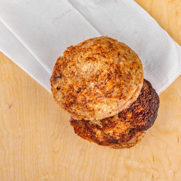 Two grilled Home Run Burger patties, one slightly charred, on a white napkin and wooden surface.