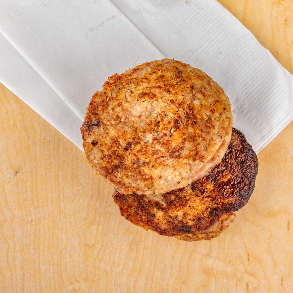 Two grilled Home Run Burger patties, one slightly charred, on a white napkin and wooden surface.