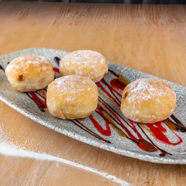 Four powdered sugar donuts with chocolate and raspberry drizzle on a gray plate.