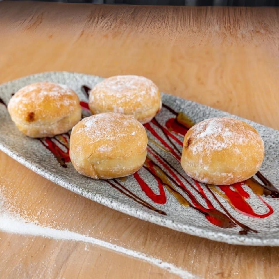 Four powdered sugar donuts with chocolate and raspberry drizzle on a gray plate.