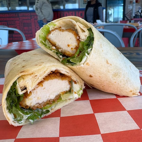 Two crispy chicken wraps with lettuce and sauce, cut in half on red and white checkered paper.