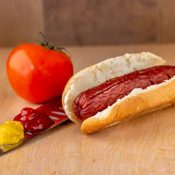 A Home Run Burger hot dog in a bun with a tomato, ketchup, and mustard on a spatula.