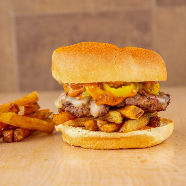 A Home Run Burger with melted cheese, peppers, sauce, and fries on a wooden surface.