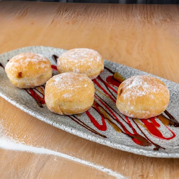 Four powdered sugar donuts with chocolate and raspberry drizzle on a gray plate.