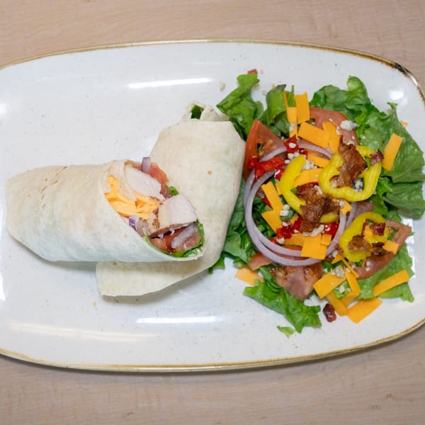 Chicken wrap with cheese, tomatoes, and onions, served with a side salad.