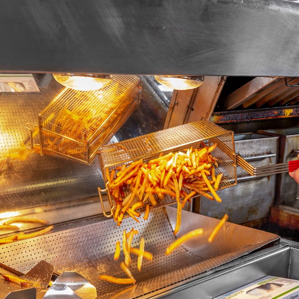 Golden french fries being poured from a metal basket into a warming tray at Home Run Burger.