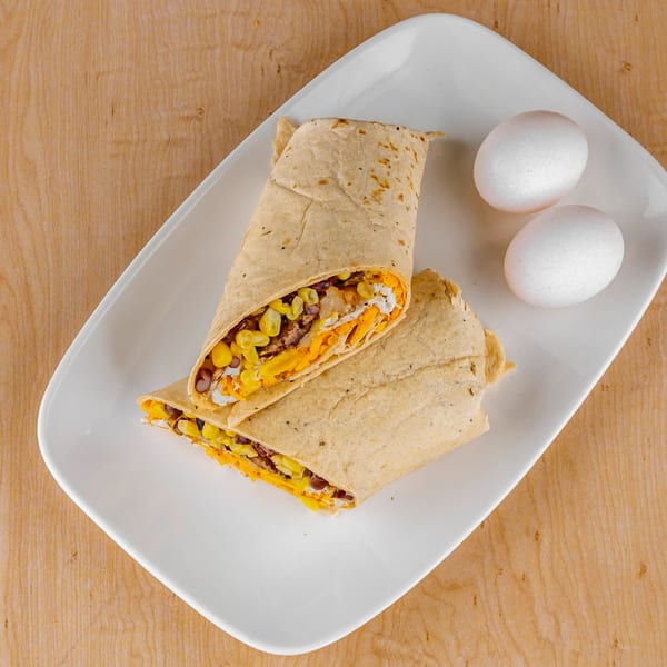 Two breakfast burritos filled with corn, beans, cheese, and eggs on a white plate.