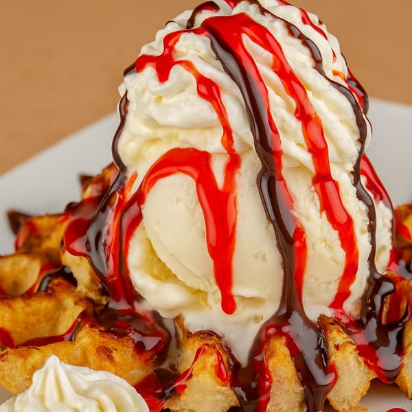 Waffle topped with vanilla ice cream, whipped cream, chocolate, and strawberry syrup.