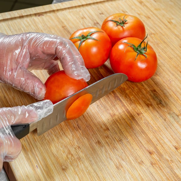 Gloved hands slicing fresh red tomatoes on a wooden cutting board for Home Run Burger.